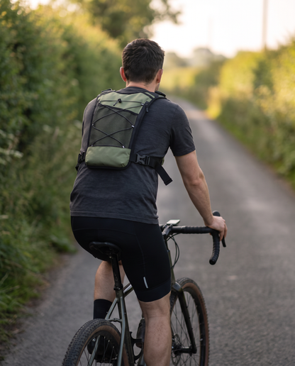 Man cycling down a country lane wearing the army green tactical chest rig, showing the mesh back pack